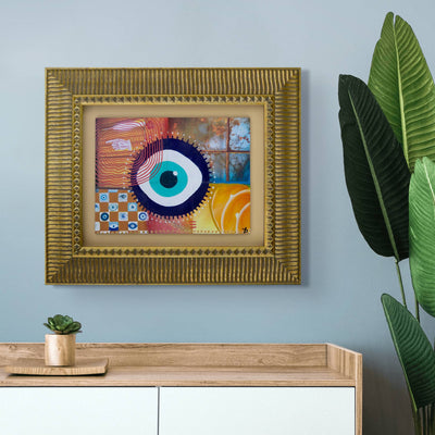 Mixed media collage original wall art with a colorful evil eye design in a gold frame on a light blue wall.