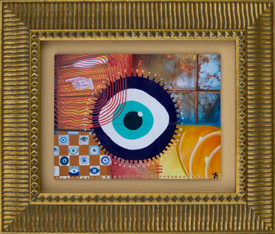 Framed mixed media collage artwork with a central evil eye design surrounded by colorful patterns in a gold frame with mat.