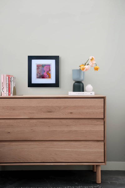 Collage artwork above a wooden dresser with decorative items against a gray wall