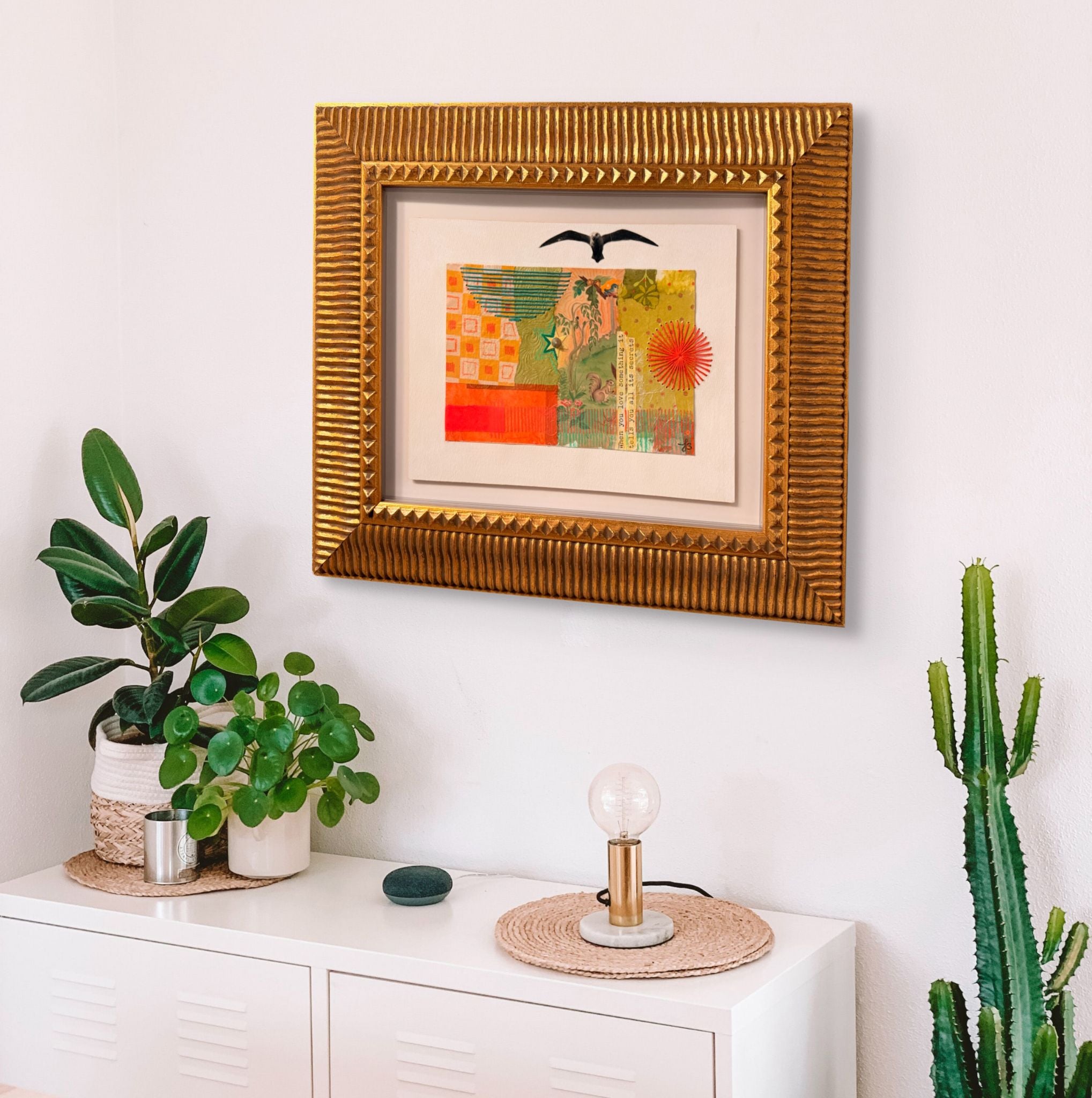 Framed artwork on a wall above a white cabinet with decorative items.