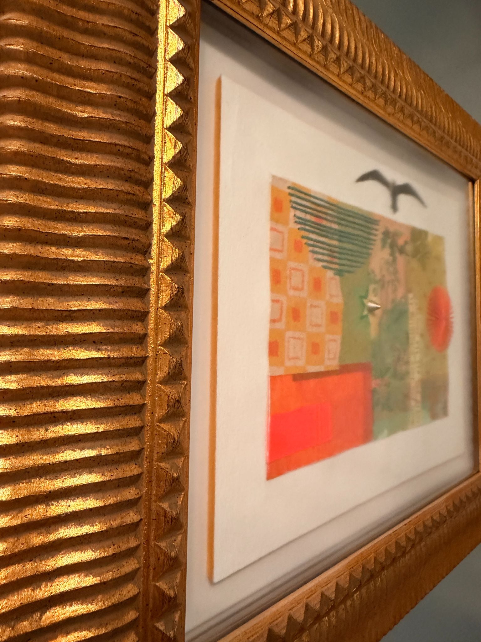 Close up shot of framed artwork with a gold frame on a textured wall.