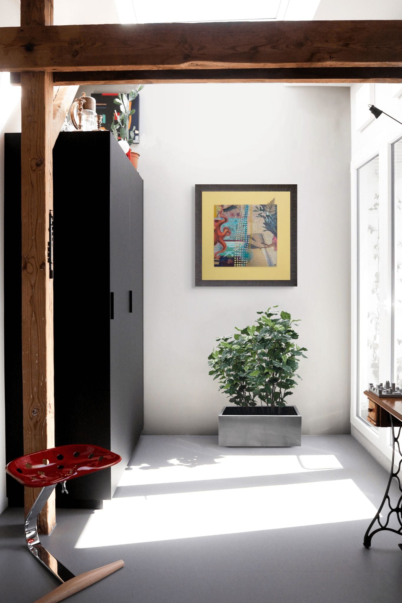 Modern interior with a plant, colorful mixed media collage art on wall, and a red chair.